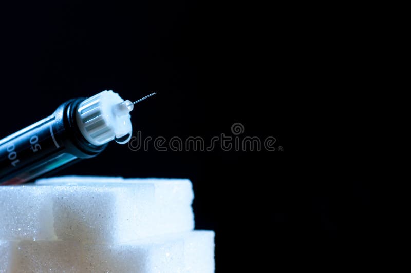 Diabetes pen with a drop of insulin on sugar cubes isolated on black.