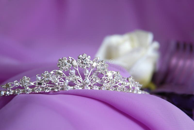 Close-up photo of the silver or platinum (white gold) diadem with diamonds on a lilac background. In the background are visible jewelry rose. Tiara for the bride. Close-up photo of the silver or platinum (white gold) diadem with diamonds on a lilac background. In the background are visible jewelry rose. Tiara for the bride.