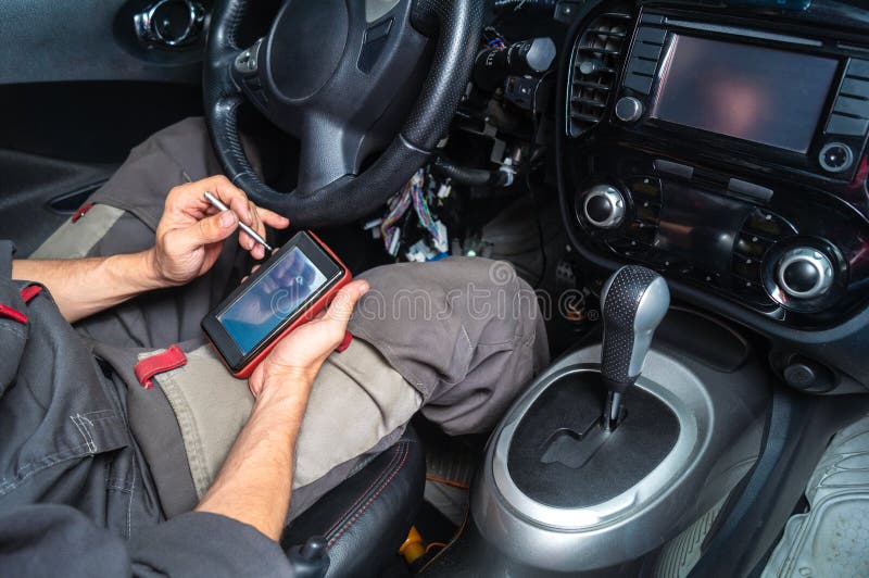 Diagnostiek van automislukkingen: een elektricien in grijze kleren zit in het auto` s binnenland en leest het probleem