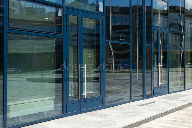 Diagonal view of modern building wall with bif glass window and door with blue frame. Street reflection.