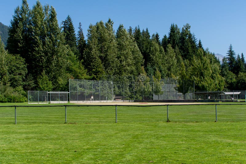 Diamante de baseball ou softball vazio da cerca traseira e linha de enfeites olhando para a grama e árvores em Whistler, Britânic imagens de stock royalty free Diamante de baseball ou softball vazio da cerca traseira e linha de enfeites olhando para a grama e árvores em Whistler, Britânic imagens de stock royalty free