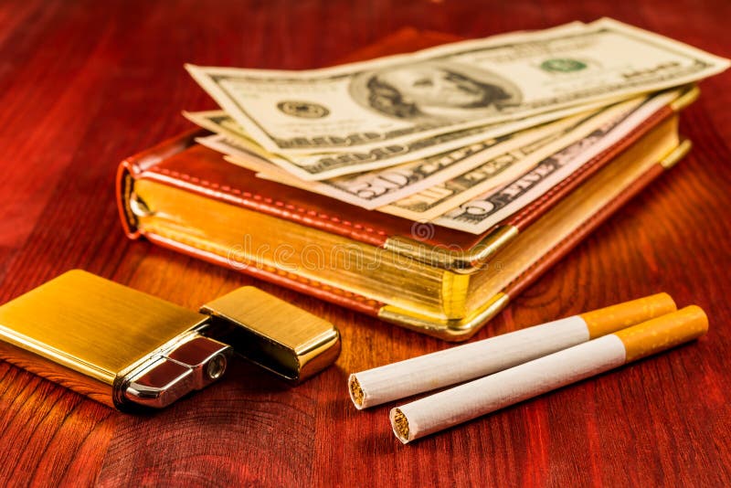 Leather diary and cigarettes with golden lighter and money on a mahogany table. Focus on the cigarettes. Leather diary and cigarettes with golden lighter and money on a mahogany table. Focus on the cigarettes