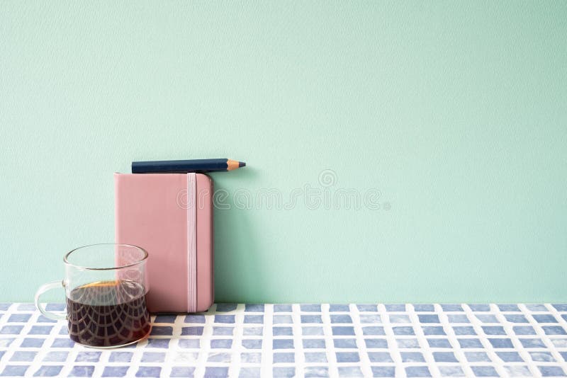 Diary notebook, pencil, coffee on blue tile desk. mint wall background. workspace. studio shot