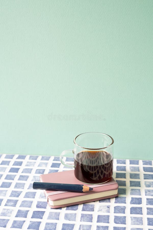 Diary notebook, pencil, coffee on blue tile desk. mint wall background. workspace. studio shot