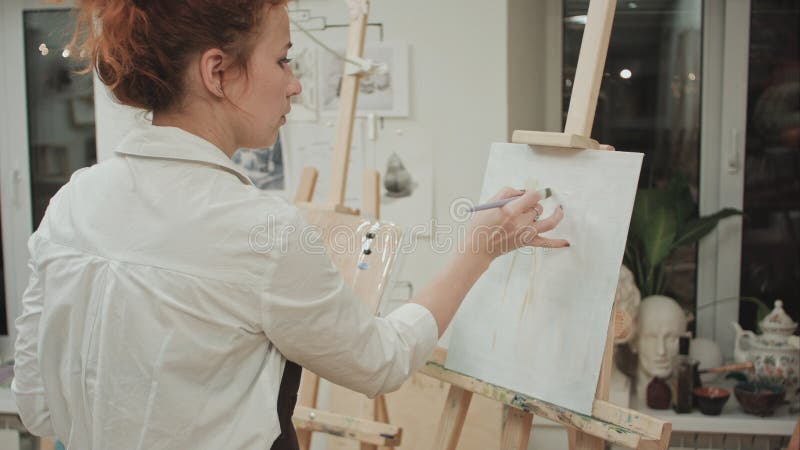 Dibujo femenino del pintor en estudio del arte usando el caballete imagen de archivo Dibujo femenino del pintor en estudio del arte usando el caballete imagen de archivo