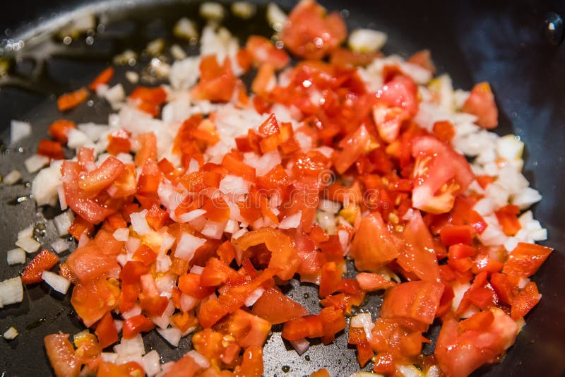 DICED TOMATOES and ONIONS BEING COOKED in FRYING PAN on OVEN. Stock