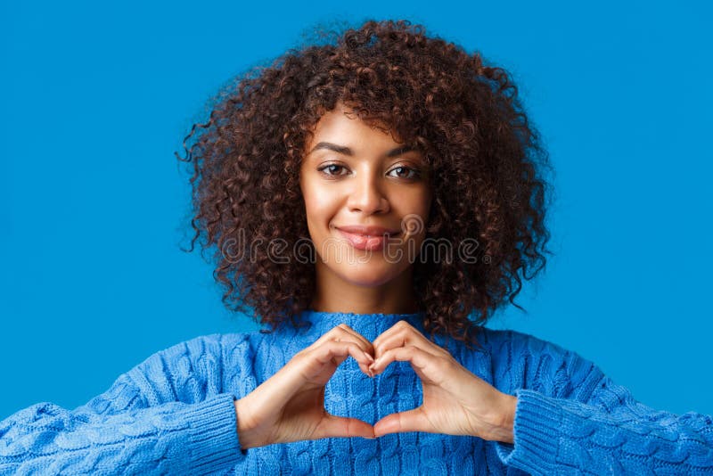 Close-up portrait tender and cute african-american romantic woman express her feelings with gesture, showing heart sign and smiling, have sympathy, confess over blue background. Close-up portrait tender and cute african-american romantic woman express her feelings with gesture, showing heart sign and smiling, have sympathy, confess over blue background.