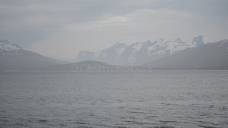 Dichter Nebel über blauer Fjordansicht mit schneebedecktem Gebirgshintergrund in der Natur des nördlichen Polarkreises