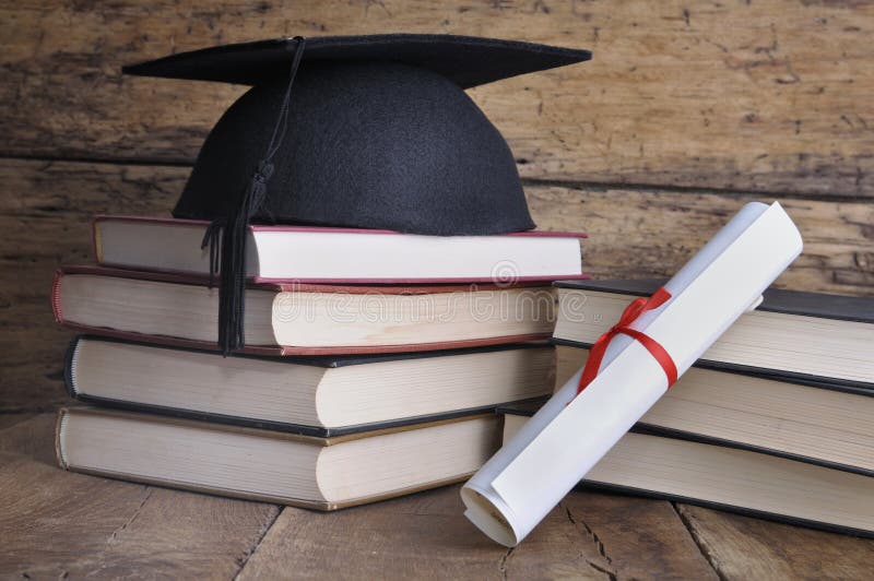 Graduate rolled up in a red ribbon and a black hat on pile of book on wooden background. Graduate rolled up in a red ribbon and a black hat on pile of book on wooden background
