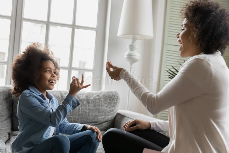 Die afrikanische kleine Tochter, die Gebärdensprache eingesetzt, kommuniziert mit Mutter. Afrikanische Behinderte Tochter und ihre Mutter, die auf Sofashowsymbolen mit den Händen mithilfe der visualmanual Fingergesten zu Hause interagieren sitzt. Verlust- der Hörfähigkeitschwerhörigegebärdensprache Schulkonzept lernt, die