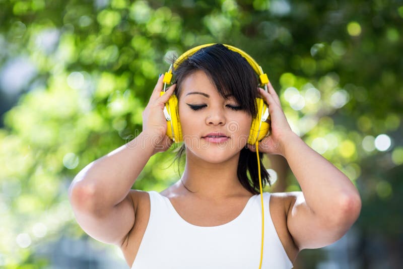 Athletic woman wearing yellow headphones and enjoying music with eyes closed in the city. Athletic woman wearing yellow headphones and enjoying music with eyes closed in the city