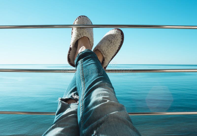 Die Beine der Frauen in heftigen Jeans und in den Pelzpantoffeln der weißen Schafe, die auf der Querlatte des Balkons liegen stockfotografie Die Beine der Frauen in heftigen Jeans und in den Pelzpantoffeln der weißen Schafe, die auf der Querlatte des Balkons liegen stockfotografie