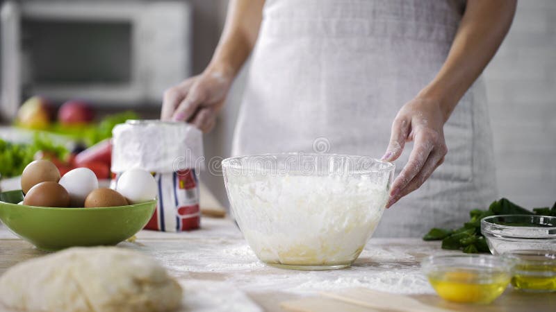 Die Bäckereiarbeitskraft, die Mehlsieb für das Hinzufügen in Glasschüssel, Pizzarezept hält, neigt sich lizenzfreies stockbild Die Bäckereiarbeitskraft, die Mehlsieb für das Hinzufügen in Glasschüssel, Pizzarezept hält, neigt sich lizenzfreies stockbild