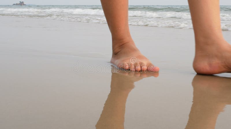Die Frauenfüße, die auf den Sand gehen, setzen mit der Welle des Meeres auf den Strand