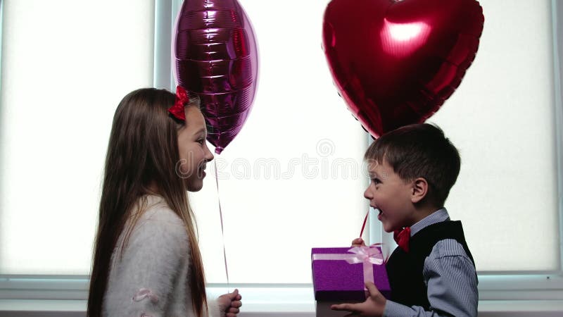 Die freundlichen Kinder, die Ballons in Form eines Herzens halten und ist in der Lage zu küssen. Mädchen gibt dem Jungen am Valent