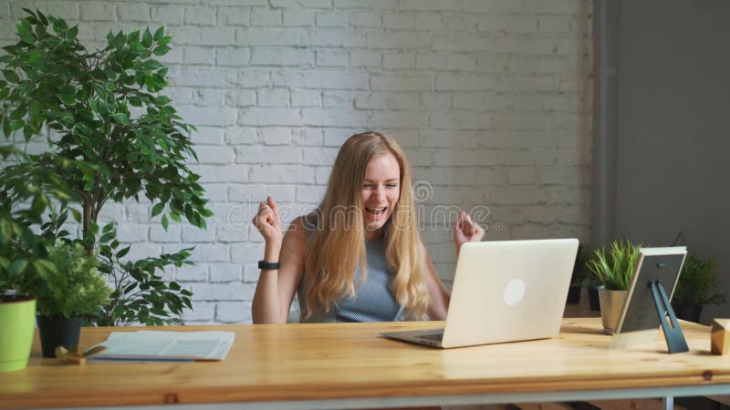 Die glückliche Frau, die aufgeregt glaubt, den Laptopschirm betrachtend, der am Arbeitsplatz sitzt, feiert Geschäftserfolg, on-li