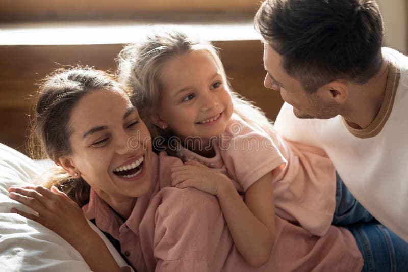 Die glückliche geweckte Familie, die gemeinsam ist, dem Bettlachen fühlt sich glücklich stockfotografie