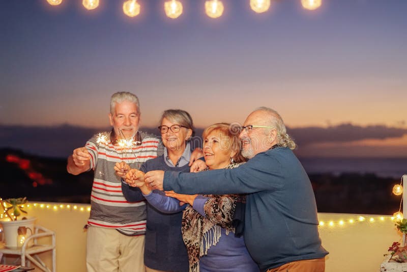 Die glücklichen älteren Freunde, die Geburtstag mit Wunderkerzen feiern, spielt im Freien - die älteren Leute die Hauptrolle Spaß stockbilder Die glücklichen älteren Freunde, die Geburtstag mit Wunderkerzen feiern, spielt im Freien - die älteren Leute die Hauptrolle Spaß stockbilder