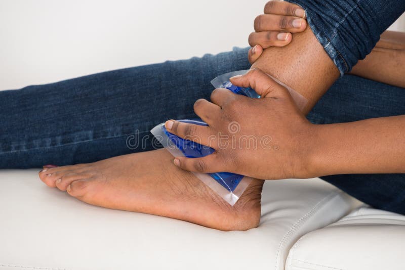 Close-up Of Person's Hand Holding Ice Gel Pack On Ankle. Close-up Of Person's Hand Holding Ice Gel Pack On Ankle