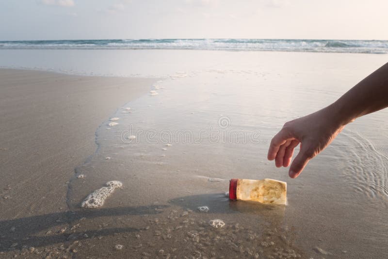 The hand of a woman is picking up a plastic bottle to clean the beach. The hand of a woman is picking up a plastic bottle to clean the beach.