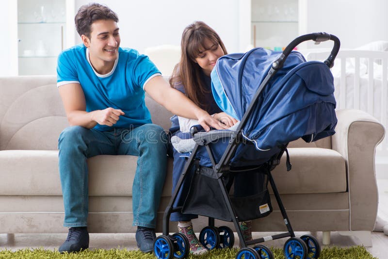 Die Junge erziehen mit ihrem neugeborenen Baby in Baby Pram, der auf dem Sofa sitzt lizenzfreies stockbild Die Junge erziehen mit ihrem neugeborenen Baby in Baby Pram, der auf dem Sofa sitzt lizenzfreies stockbild
