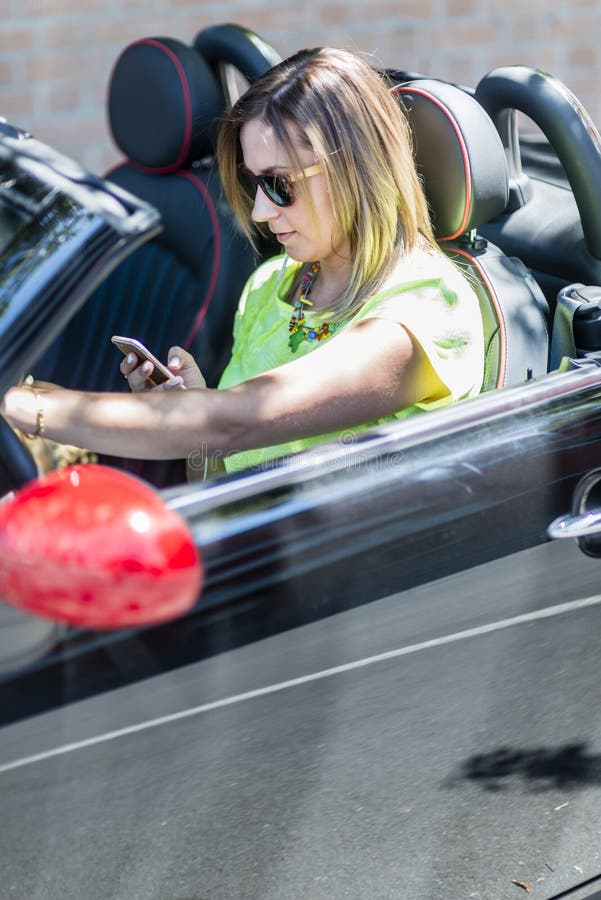 Die junge Frau, die ein Cabrioletauto fährt, lenkte mit ihrem Telefon ab stockfotos Die junge Frau, die ein Cabrioletauto fährt, lenkte mit ihrem Telefon ab stockfotos