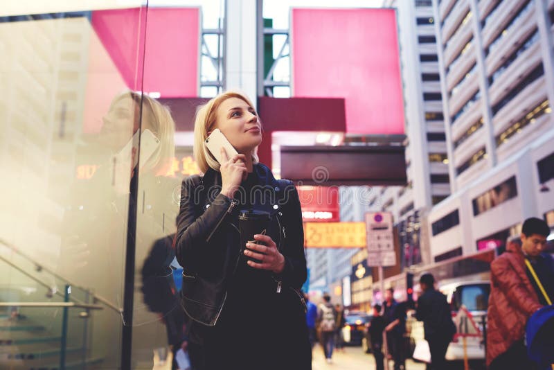 Attractive young female hipster taking part in university student exchange walking on Chinese town street having phone conversation with coach asking questions to. Attractive young female hipster taking part in university student exchange walking on Chinese town street having phone conversation with coach asking questions to