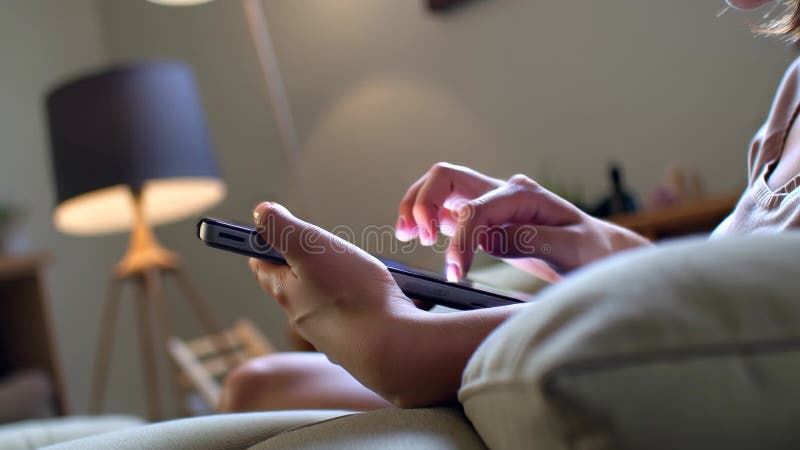 Die KI generierte Frau mit einem Smartphone, während sie sich auf einem gemütlichen Sofa in einem weich beleuchteten Wohnzimmer en lizenzfreie abbildung