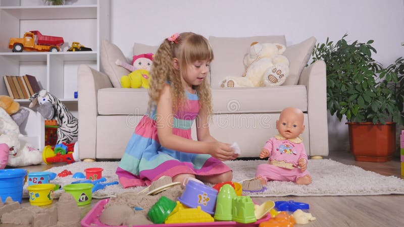 Die Kinder, die Spiel als genanntes Muttertochterspiel ein Mädchen spielen, zieht Puppe mit Plastiklöffel ein