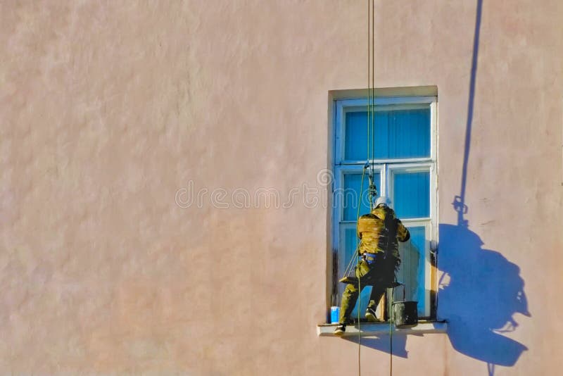 Die Mannarbeitskraft, die an der Baustelle mit Sturzhelm und an der Uniform für äußeres Gebäude der Arbeiten klettert stockbild Die Mannarbeitskraft, die an der Baustelle mit Sturzhelm und an der Uniform für äußeres Gebäude der Arbeiten klettert stockbild