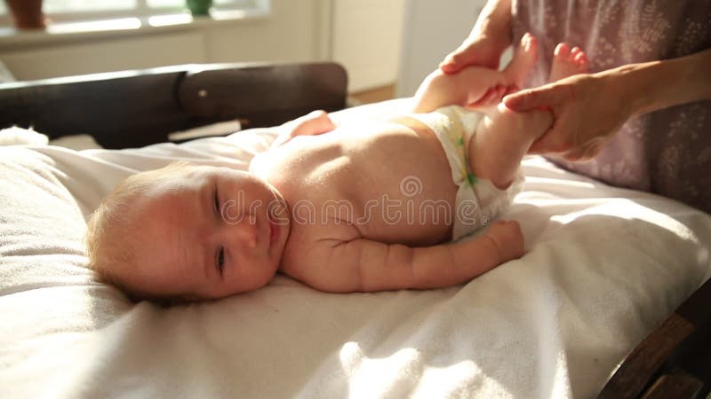 Die Mutter, die Übungen für ihr neugeborenes kleines Baby tut- erweitert seine Beine aus