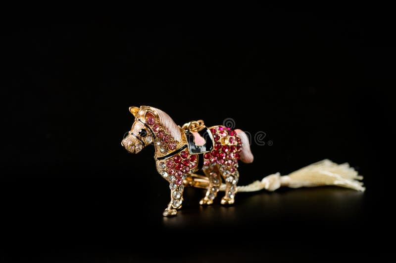Die Schlüsselkette des Pferdefiguren-Souvenirs in goldener Farbe mit hellen Kieseln auf dunklem Hintergrund lizenzfreie stockfotos Die Schlüsselkette des Pferdefiguren-Souvenirs in goldener Farbe mit hellen Kieseln auf dunklem Hintergrund lizenzfreie stockfotos