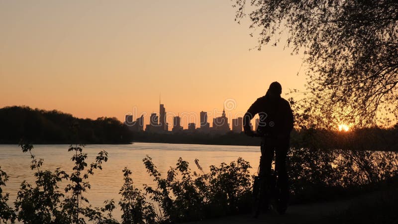 Die Silhouette eines Radfahrers vor dem Hintergrund des abendlichen Warschauer. eine große Stadt bei Sonnenuntergang.