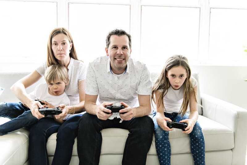Die vierköpfige Familie, die Spaß auf dem Sofa spielen hat zu Hause, Videospiel lizenzfreie stockfotografie Die vierköpfige Familie, die Spaß auf dem Sofa spielen hat zu Hause, Videospiel lizenzfreie stockfotografie