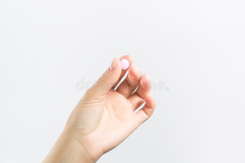 Die weibliche Hand hält eine runde rosa Pille auf weißem Hintergrund stockfoto