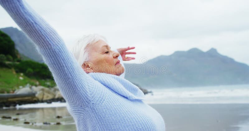 Die ältere Frau, die mit den Händen steht, hob auf Strand an
