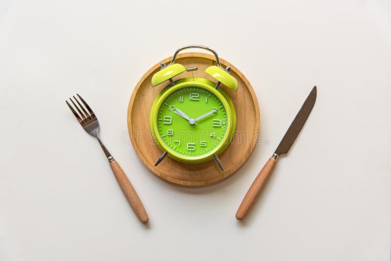 Diet and weight loss for healthy intermittent fasting lunchtime . Alarm clock and plate with cutlery on concrete background. Diet and Healthy Concept. Diet and weight loss for healthy intermittent fasting lunchtime . Alarm clock and plate with cutlery on concrete background. Diet and Healthy Concept