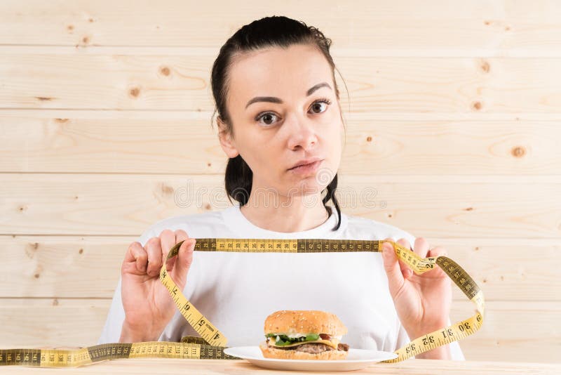 Dieta La donna del ritratto vuole mangiare un hamburger ma la bocca attaccata dello skochem, il concetto della dieta, gli aliment immagine stock Dieta La donna del ritratto vuole mangiare un hamburger ma la bocca attaccata dello skochem, il concetto della dieta, gli aliment immagine stock