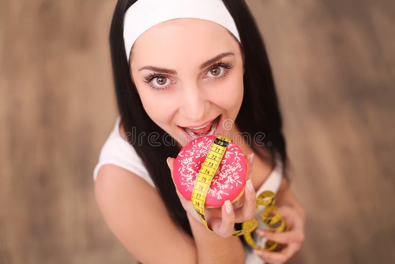 Dieta Peso corporal de medição da mulher na escala de peso que guarda a filhós Os doces são comida lixo insalubre Fazendo dieta, imagem de stock Dieta Peso corporal de medição da mulher na escala de peso que guarda a filhós Os doces são comida lixo insalubre Fazendo dieta, imagem de stock