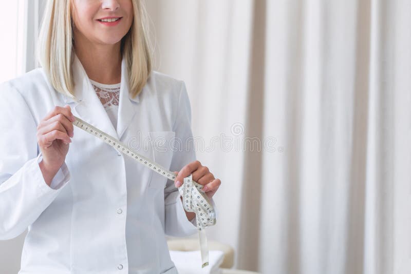 Dietista de pelo rubio con uniforme blanco que sostiene un centímetro de sastre