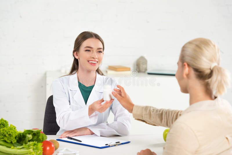 Dietititer i vit rock som ger tabletter till patienten vid bordet royaltyfria bilder
