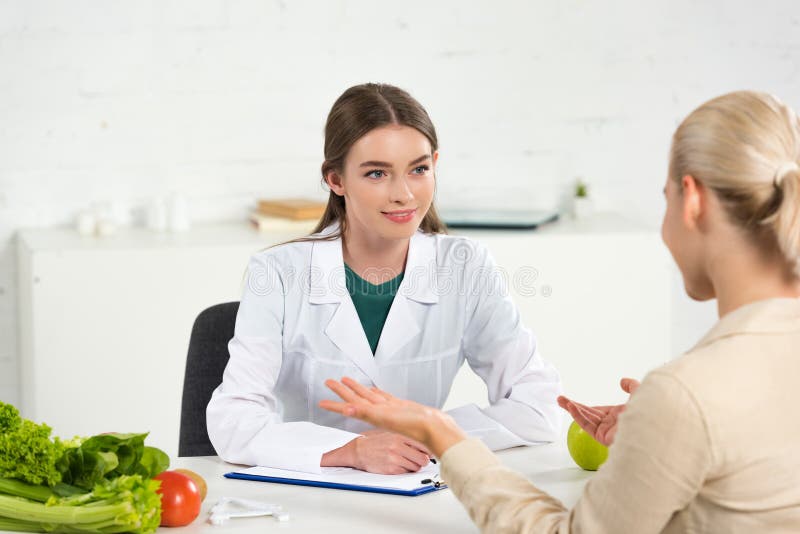 Dietititer i vit rock som tittar på patienten vid bordet royaltyfri bild