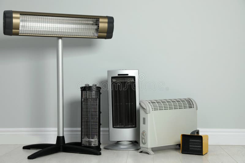 Different electric heaters near light grey wall indoors. Space for text stock photos