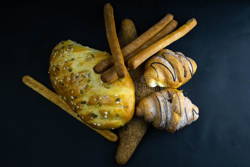 Different kinds of fresh bread with grain on black rustic background stock photography