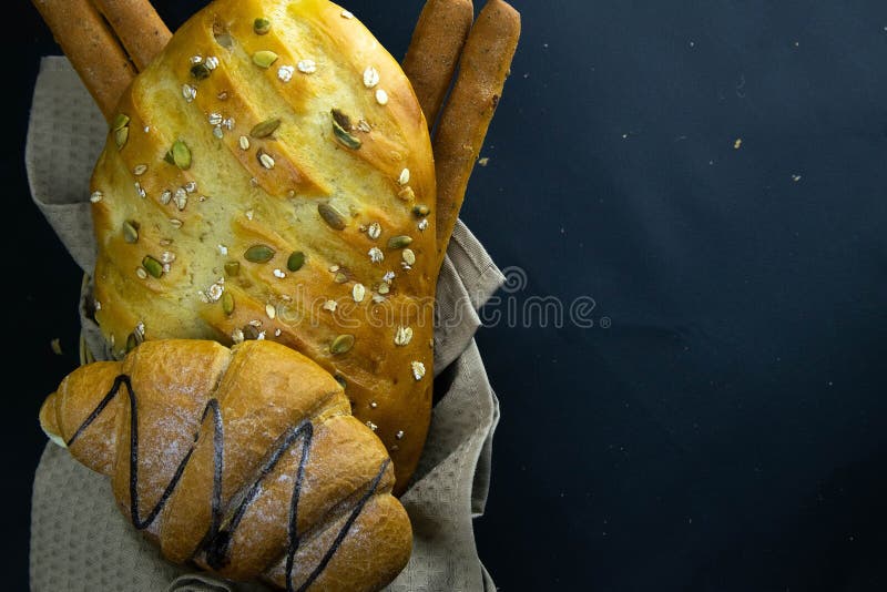 Different kinds of fresh bread with grain on black rustic background royalty free stock images