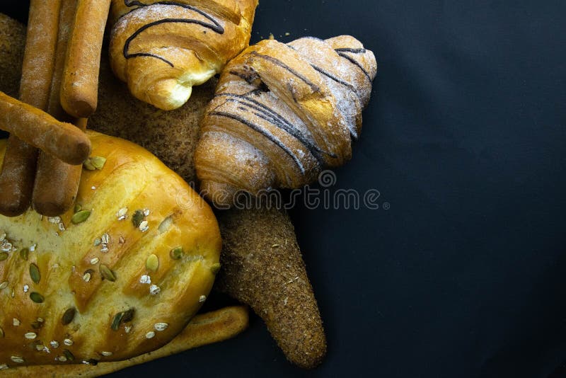 Different kinds of fresh bread with grain on black rustic background stock photo