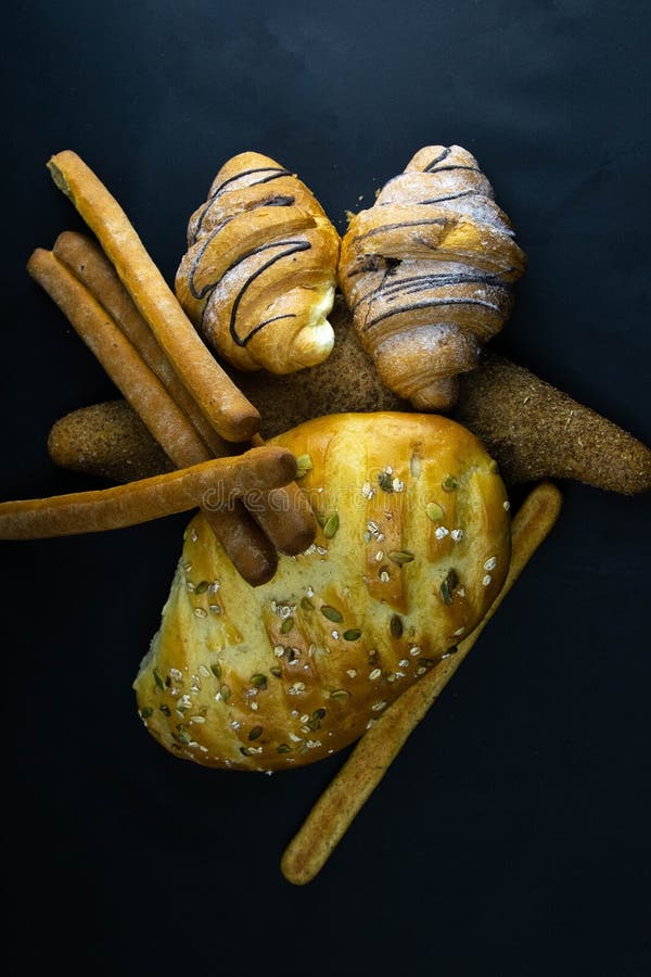 Different kinds of fresh bread with grain on black rustic background royalty free stock photos