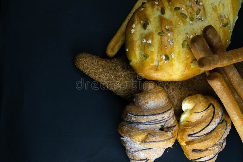 Different kinds of fresh bread with grain on black rustic background stock photo