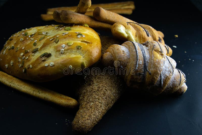 Different kinds of fresh bread with grain on black rustic background stock image
