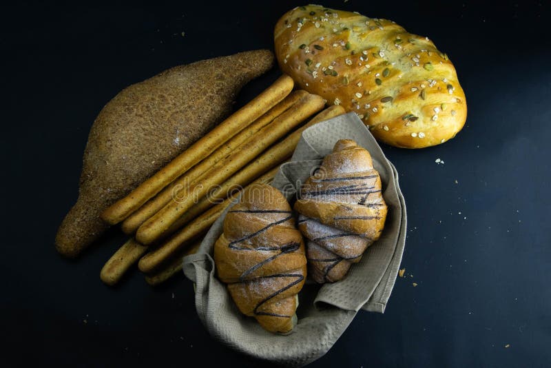 Different kinds of fresh Croissant and bread with grain on black rustic background royalty free stock photography